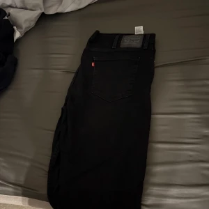 Svarta jeans från Levi's - Säljer ett par svarta 514 jeans från Levi's med klassisk femficksdesign och rakt snitt. Byxorna har en diskret röd Levi's-tag på bakfickan och svart läderpatch i midjan. Perfekta till många olika outfits. W38 L32