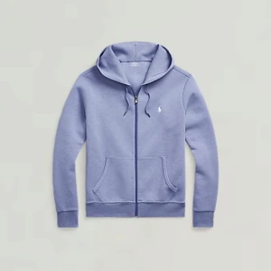 Blå hoodie från Polo Ralph Lauren - Säljer en blå hoodie från Polo Ralph Lauren med dragkedja och huva. Tröjan har två fickor framtill och en broderad vit logga på bröstet. Perfekt för en avslappnad stil och enkel att matcha med det mesta. Köpt för 2199kr