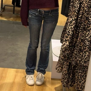 Lågmidjade jeans american eagle  - Snygga blå jeans från American Eagle med slim bootcut-passform. Jeansen har klassiska fem fickor, låg midja och diskreta slitningar framtill. Perfekta för dig som gillar en smal men ändå lite utsvängd look. Stängs med dragkedja och knapp.