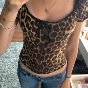Leopardmönstrad topp med rosett från Romwe - Säljer en leopardmönstrad topp från Shein i storlek XS. Toppen har korta ärmar, söt rosettdetalj framtill och svarta spetsdetaljer vid halsringningen. Materialet är stretchigt och figurnära.