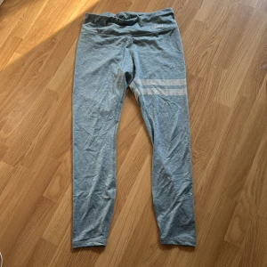 Gråblå träningstights från Stronger - Snygga gråblå tights från Stronger med två reflekterande ränder på ena benet och diskreta prickdetaljer bak. Perfekta för träning och har en hög midja för extra komfort.