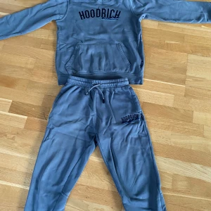 Grå mjukis dress från Hoodrich. - Säljer en grå mjukis dress från Hoodrich med svart tryck på bröstet. Tröjan har en stor magficka och långa ärmar med ribbade muddar. Perfekt för en avslappnad stil. Storlek på tröjan är 13-15 år och storlek på byxorna är 12-13 år. Pris kan diskuteras 