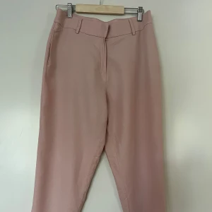 Linnebyxor, H&M, 40, rosa - Eleganta, ljusrosa byxor med en avslappnad passform från H&M. Byxorna har en klassisk design med fickor och en smickrande silhuett. Elastisk i midjan. Storlek 40. 52% linme och 48% viskos. Nyskick.  Mått: Midja ca 40 cm Stuss 48 cm Längd yttre ca 94 cm Längd inre ca 63 cm