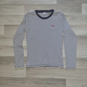 Randig långärmad tröja från Levi's - Säljer en svartvit randig långärmad tröja från Levi's med rund halsringning och liten röd Levi's-logga på bröstet. Tröjan är i bomull och har en klassisk, tidlös look som passar till det mesta.
