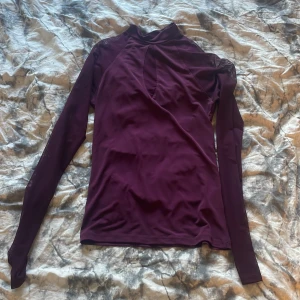 Vinröd/lila långärmad omlottopp - Säljer en vinröd/lila långärmad topp med hög hals. Tunnare material som sitter snyggt på kroppen och passar perfekt till många olika outfits.