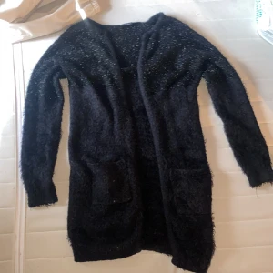 Svart fluffig och glittrig kofta med fickor - Fluffig öppen koftan med små fickor framtill och glittrig upptill