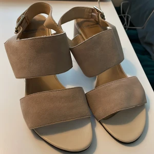 Beige klackade sandaler från Vagabond - Säljer ett par snygga beige sandaler från Vagabond med breda remmar och öppen tå. Skorna har en stabil klack, spänne vid ankeln och är tillverkade i skinn. Perfekta för dig som vill ha både stil och komfort. Endast använta vid två tillfällen. Klacken är 8cm hög 