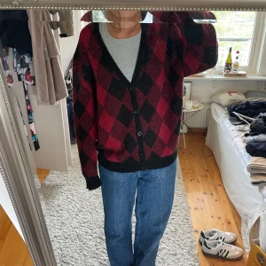 Rutig kofta i vinrött och svart från Sweet Skibs - Säljer en mysig kofta från Sweet Skibs i vinrött och svart med rutigt mönster. Koftan har knappar framtill, v-ringning och långa ärmar. Perfekt att slänga på sig över en t-shirt eller linne. Funkar för både killar och tjejer!