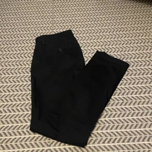 Svarta chinos från GAP - Säljer ett par svarta chinos från GAP i modellen Essential Khaki Slim. Byxorna har en slim passform och klassisk design med knapp och dragkedja i midjan. Perfekta för en stilren och enkel look.