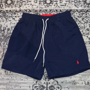 Marinblå badshorts från Polo Ralph Lauren - Säljer ett par marinblå badshorts från Polo Ralph Lauren, dem är små i passform så jag säljer dem som storlek S. Dem är perfekta för stranden eller poolen!
