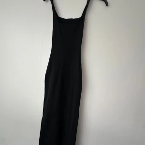 Svart långklänning med smala axelband - En stilren svart långklänning med smala axelband och rak passform. Perfekt för dig som gillar minimalistisk stil och vill ha en enkel men snygg klänning till garderoben.