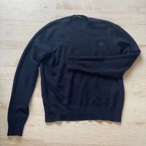 Mörkblå stickad tröja från Acne Studios - Säljer en stilren mörkblå stickad tröja från Acne Studios. Tröjan har rund halsringning och långa ärmar. Perfekt för dig som gillar minimalistisk design och vill ha något klassiskt i garderoben. Skickar dagen efter du köper! Har ett litet hål (kan säkert fixas) men man ser det knappt!