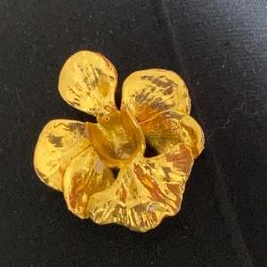 Guldpläterad orkidé brosch  - Säljer en exklusiv guldpläterad brosch från Risis i form av en orkidé . Broschen har en vacker, organisk form med detaljerade blomblad och en elegant glansig finish. Perfekt som accessoar för att lyfta din outfit.