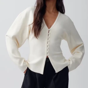 Vit kofta med knappar från Gina Tricot - Säljer en stilren vit kofta från Gina Tricot med v-ringning och knappar framtill. Koftan har lång ärm och är tillverkad i ett mjukt, slätt material. Perfekt att styla med både jeans och kjol. Helt ny endast testad