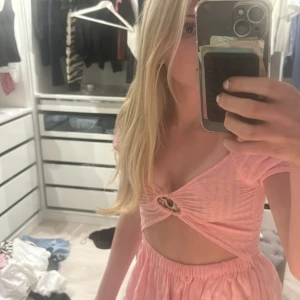 Rosa klänning med cut-out och puffärmar - Säljer en söt rosa klänning med puffärmar och smockad överdel. Klänningen har en snygg cut-out detalj framtill och baktill med knut, samt volang i kjolen. Perfekt för sommarens tillfällen!