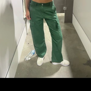 Gröna cargopants med raka ben - Säljer ett par gröna cargopants med raka ben och flera fickor på sidorna. Byxorna har normal passform och stängs med knappar och dragkedja. Storlek 38
