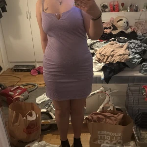 Ljuslila blommig kortklänning från JDY - Säljer en söt ljuslila kortklänning från JDY med smala axelband och små vita blommor som mönster. Klänningen har en liten v-ringning framtill med dekorativ knytning. Perfekt för sommarens varma dagar!