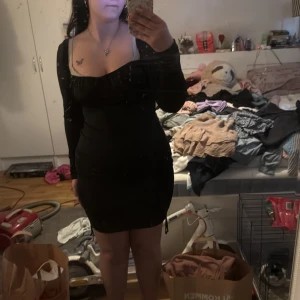 Svart tight långärmad klänning med knyt - Säljer en svart, tight klänning med långa ärmar och söt knyt-detalj i sidan. Klänningen har en snygg v-ringning och figurnära passform som framhäver siluetten. Perfekt för dig som gillar en enkel men stilren look.