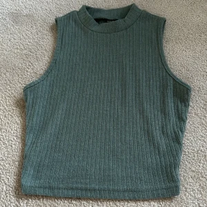Grön ribbad ärmlös topp från SHEIN - Snygg grön ribbad topp från SHEIN i storlek XS. Modellen är ärmlös med hög hals och croppad passform, perfekt till sommaren. Enkel att matcha med både jeans och kjol.