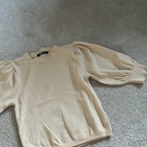 Beige tröja med puffärmar från Gina Tricot - Säljer en beige tröja från Gina Tricot med puffiga långärmar och rund halsringning. Tröjan har en mjuk och bekväm känsla, perfekt för att lyfta en enkel outfit. Passar dig som gillar stilrena plagg med en twist.