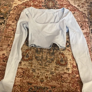 Ljusblå croppad långärmad topp - Säljer en ljusblå croppad topp med lång ärm och fyrkantig ringning. Toppen är ribbad och har en tight passform, perfekt att styla med höga jeans eller kjol.
