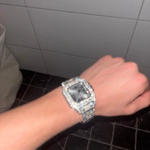 Lyxig fyrkantig klocka - Säljer en glittrig klocka med fyrkantig urtavla och armband i silverfärg, täckt av gnistrande stenar. Klockan har en klassisk design med romerska siffror på urtavlan och passar perfekt som accessoar. Reservlänkar tillkommer.