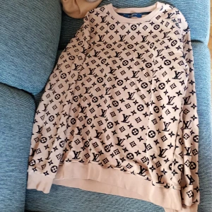 Beige Louis Vuitton sweatshirt med monogram stl XL - Säljer en beige sweatshirt från Louis Vuitton med klassiskt svart monogrammönster över hela tröjan. Tröjan har rund halsringning och långa ärmar. Perfekt för dig som gillar lyxiga streetwear-vibbar.