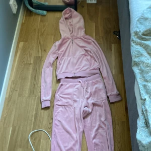 Rosa mjukisbyxor med matchande hoodie - Det här är inte samma sett som den andra jag säljer, den här är minde och har lite mörkare färg. Säljer ett par rosa mjukisbyxor i velour med resår och snörning i midjan samt fickor med lock bak. Byxorna har en loose passform och matchas med en hoodie i samma material och färg. Vi kan diskutera pris. Det är inga fläckas och det är från barn sidan.