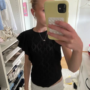 Svart blus med volangärmar - Säljer en svart blus med korta volangärmar och diskret rutmönster. Blusen har en feminin och luftig känsla, perfekt till sommaren. Passar till både jeans och kjol.