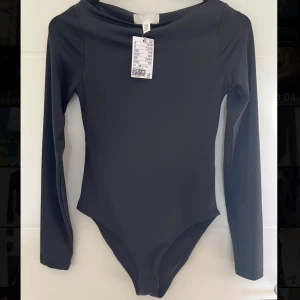 Svart långärmad bodysuit från H&M - Säljer en svart långärmad bodysuit från H&M som aldrig använts. Den har en tight passform och är tillverkad i ett stretchigt syntetmaterial. 