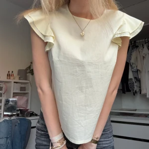 Ljusgul blus med volangärmar  - Supersöt ljusgul blus från lindex med volangdetaljer på axlarna. Blusen är ärmlös med rund halsringning och har en rak passform. Perfekt att styla med jeans eller kjol för en fräsch look perfekt i sommar!!! 🌸💕