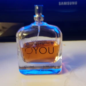 Stronger With You parfymflaska - En elegant parfymflaska med texten 'Stronger With You'. Flaskan är genomskinlig med rundade kanter och innehåller en bärnstensfärgad vätska. Spraykork i silverfärg. Perfekt för dig som gillar stilrena och moderna dofter.