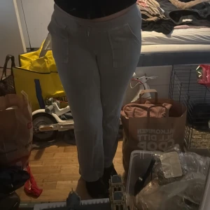 Grå mjukisbyxor från Juicy Couture - Grå mjukisbyxor från Juicy Couture med fickor framtill och bakfickor med lock och knappar. Byxorna har resår i midjan och är i mjukt bomullsmaterial. Perfekta för en avslappnad stil.