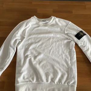 Vit sweatshirt från Stone Island - Säljer en stilren vit sweatshirt från Stone Island med klassisk patch på vänster ärm. Tröjan har rund halsringning, långa ärmar och ribbade muddar vid ärmslut och nederkant. Perfekt för en clean och avslappnad look. 100% äkta sälj för 900 kr, säljer den för den har blivit för liten för mig, pris kan diskuteras👍. Hör av er vid minsta fundering 