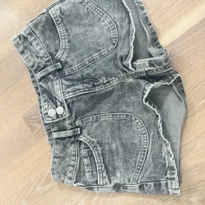 Grå low waist jeansshorts med broderade bakfickor, från Lindex - Sååå snygga och väldigt unika gråa jeansshorts från Lindex med tvättad look och dekorativa broderier på bakfickorna. Shortsen har låg midja, dragkedja och dubbla knappar framtill samt fickor både fram och bak. De är i barnstorlek men passade mig förra sommaren så skulle säga att de är som en xxs/ 30 eller 23 i jeansstorlek. Använda mindre än fem gånger. De går att justera i midjan.