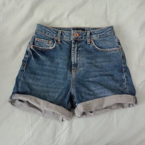 Blå jeansshorts - Snygga blå jeansshorts från Pieces med klassisk femficksdesign och uppvikta benslut. Shortsen har normal passform och stängs med knapp och dragkedja. Perfekta för varma dagar och enkla att matcha med olika toppar.