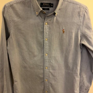 Ljusblå skjorta från Ralph Lauren - Säljer denna ljusblå skjorta från Ralph Lauren i slim fit. Fick skjortan i födelsedagspresent så att skjortan är bara testad men aldrig använd då den var för liten för mig.skjortan är storlek M men skulle säga att den sitter som S.