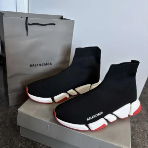 Balenciaga Speed Trainer sneakers - Säljer ett par svarta Balenciaga Speed Trainer sneakers med vit och röd chunky sula. Skorna har en strumpliknande passform och Balenciaga-logga på sidan. Perfekta för dig som gillar en modern och sportig look.