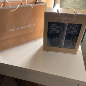 Svarta fluffiga sandaler från Michael Kors - Svarta sandaler från Michael Kors med fluffig insida och bred rem framtill. Remmen har ett svartvitt mönster med MK-logga över. De passar perfekt nu till sommaren! 💗De är endast använda inomhus men de funkar lika bra för utomhusbruk. Köpte de för ca 1 år sen och de är väl använda. Pälsen är lite tufsig som det brukar bli efter ett tag men det ser man bra på bilderna. Kartong tillkommer 💕det tillkommer även extra stenar som man kan sätta på ifall någon Sten skulle åka av, vilket det inte gjort än