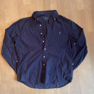 Mörkblå skjorta från Ralph Lauren - Klassisk mörkblå skjorta från Ralph Lauren med ljus blå broderad logga på bröstet. Perfekt till våren och sommaren ☀️ Storleken är L Classic fit och personen på bilden är 184. 🙌Mycket lite använd och inga synliga fläckar✅