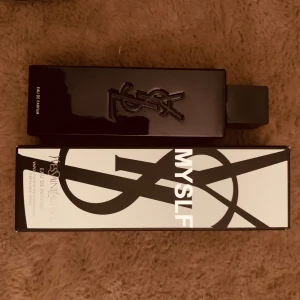 Yves Saint Laurent MYSLF Eau de Parfum - Säljer en elegant parfym från Yves Saint Laurent, MYSLF Eau de Parfum. Flaskan är svart och rektangulär med YSL-loggan i relief på framsidan. Kommer i en stilren svartvit kartong med grafisk design.