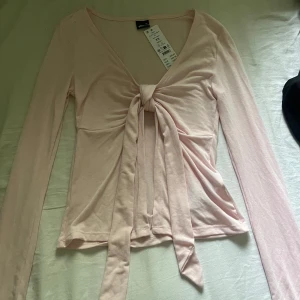 Ljusrosa långärmad topp med knyt - Säljer denna fina ljusrosa långärmade topp med knytning. Aldrig använd