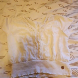 Vit blus med v-ringning och spetsdetaljer - Säljer en söt vit blus från Ü i storlek 146/152. Blusen har v-ringning, korta ärmar och fina spetsdetaljer längs halsringningen. Den har bred resår nertill för en snygg passform. Perfekt till stranden!❤️