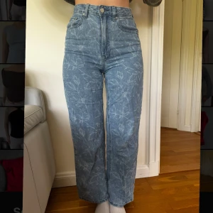 Blå mönstrade jeans med raka ben - Säljer ett par blå jeans med diskret bladmönster och raka ben. Byxorna har hög midja, klassisk femficksdesign och stängs med dragkedja och knapp. Perfekta för dig som vill ha något unikt men ändå stilrent.