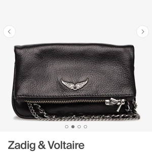 Svart axelväska med kedja - Snygg svart Zadig axelväska med kedjedetaljer och ett coolt vingmotiv på framsidan. Väskan har en dragkedja för säker förvaring och en stilren design som passar perfekt för en kväll ute.