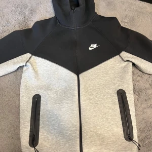 Nike Tech Fleece hoodie - Nike Tech Fleece hoodie i svart och ljusgrått med dragkedja och två stora fickor framtill. Aldrig använd i utmärkt kvalitet