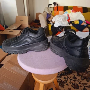 Chunky svarta sneakers med platåsula - Säljer ett par chunky svarta sneakers med kraftig platåsula och snörning. Skorna har en sportig vibe och är tillverkade i syntetmaterial med rund tå. Perfekta för dig som gillar streetstyle och vill ha extra höjd.