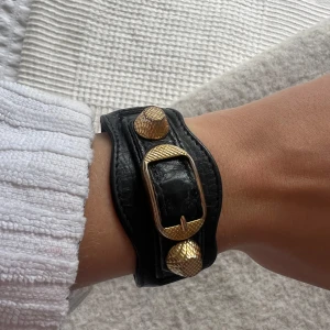 Svart armband från Balenciaga med gulddetaljer - Säljer mitt jätte fina armband från Balenciaga med snygga guldfärgade detaljer och spänne. Verkligen skit snyggt och lyfter en hel outfit!!! Kommer med box och äkthetsbevis (sista bilden) ♥️♥️♥️