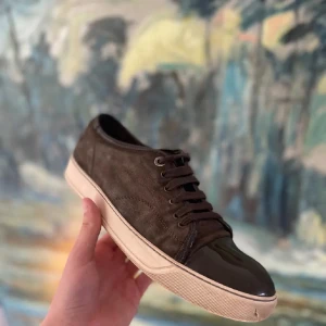 Lanvin - Säljer ett par mörk grå sneakers från Lanvin med snygg lackad tå och vita sulor. Skorna har snörning och en klassisk rund tå. Perfekta för dig som vill ha en stilren och exklusiv look till vardags. De finns en defekt på glansen som ni ser. Men annars är dom i helt ok skick🙌 kan gå ner vid snabb affär👌🏼