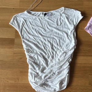 Vit kortärmad topp från Divided - Säljer en vit kortärmad topp från Divided. Toppen har en enkel design med rund hals och är tillverkad i ett mjukt material. Perfekt för en avslappnad stil.